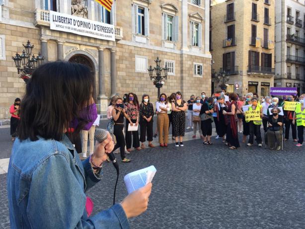 Una dona d'esquenes parlant amb un micròfon i gent concentrada a la plaça