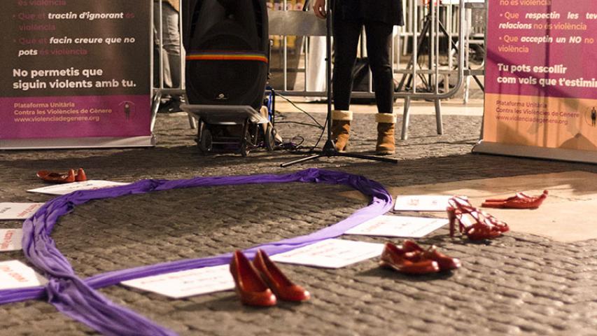 Cartells on s'indica què és violència i què no és violència de fons, una dona fent un parlament davant un micròfon i sabates veremlles en primer plànol