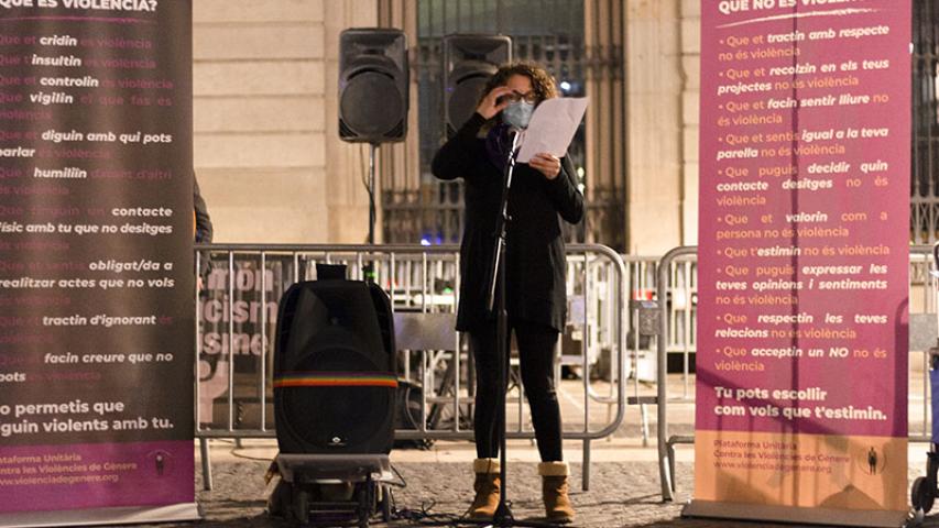 Cartells on s'indica què és violència i què no és violència de fons, una dona fent un parlament davant un micròfon i sabates veremlles en primer plànol